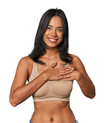 Fototapeta premium Young Filipino woman in light wear has friendly expression, pressing palm to chest. Love concept.