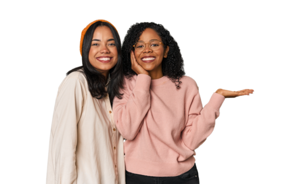 Young Latin friends together in studio holds copy space on a palm, keep hand over cheek. Amazed and delighted.
