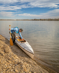 senior male paddler with expedition decked canoe on a lake shore in early spring, Boedecker...