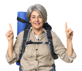 Caucasian mid-age female with hiking gear indicates with both fore fingers up showing a blank space.