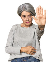 Caucasian mid-age female on studio background standing with outstretched hand showing stop sign,...