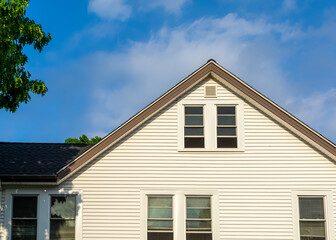 Upper portion of a family house with white siding against a blue sky with scattered clouds, Brighton, Massachusetts, USA