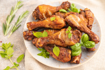 Smoked chicken legs on a ceramic plate on a brown concrete background. Side view, selective focus