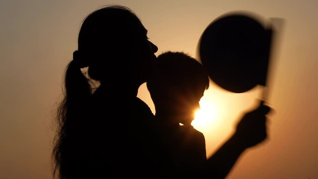 An Asian boy and her mom sitting under the hot sun trying to cool her body using a hand fan.