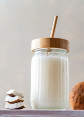 A jar of fresh coconut milk with a bamboo straw, accompanied by stacked coconut slices and a whole coconut on a textured surface.