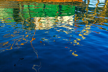 Harbors objects reflecting on dark blue water, creating an abstract-like composition