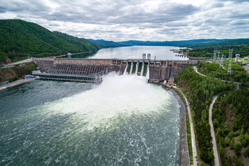 Aerial view of concrete dam releasing water into river on cloudy day. Water discharge at...