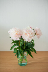 Bouquet of pink peonies in glass vase on wooden chest of drawers on white background. Spring flowers.