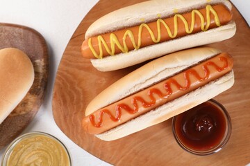 Tasty hot dogs with ketchup and mustard on white table, flat lay
