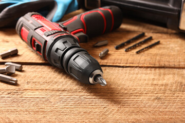 Electric screwdriver with bits and drills on wooden table, closeup