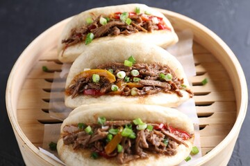 Delicious gua bao in bamboo steamer on black table, closeup