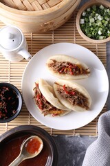 Delicious gua bao (pork belly buns), green onion and sauce on grey textured table, flat lay