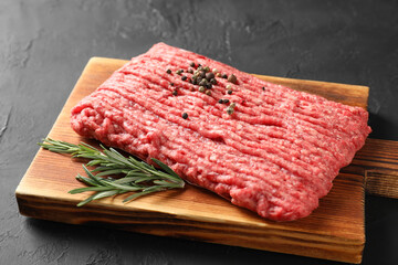 Raw ground meat, rosemary and peppercorns on black table