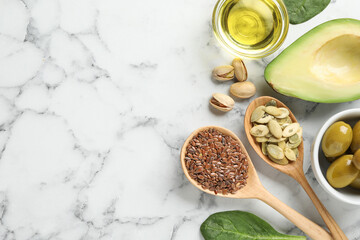 Different products and seeds high in healthy fats on white marble table, flat lay. Space for text