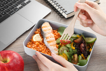 Woman eating healthy products high in vegetable fats near laptop at wooden table, closeup