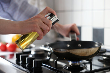 Vegetable fats. Woman sprinkling oil into frying pan on stove in kitchen, closeup