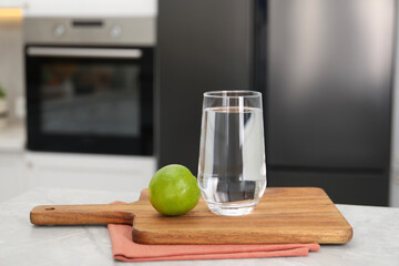 Filtered water in glass and lime on light table in kitchen