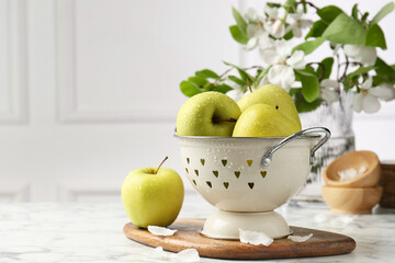 Colander with fresh apples and flower petals on white marble table, space for text