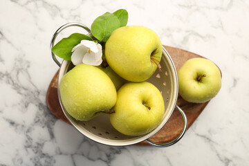Colander with fresh apples and beautiful spring blossom on white marble table, top view