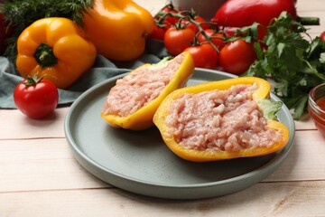 Raw stuffed peppers with ground meat and ingredients on light wooden table
