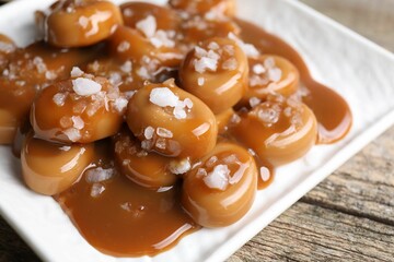 Tasty candies, caramel sauce and salt on wooden table, closeup