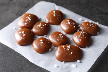 Tasty caramel candies and salt on grey table