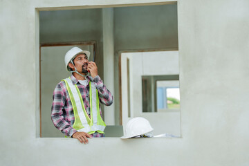 Asian male construction worker wearing hard hat and reflective vest communicating on walkie-talkie,...