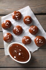 Tasty candies, caramel sauce and salt on wooden table, top view