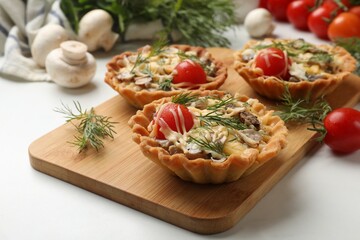 Tasty tartlets with cheese, tomatoes, mushrooms and dill on white table, closeup