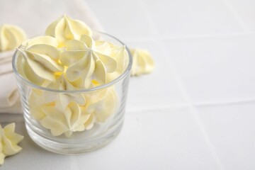 Tasty meringue cookies in glass on white tiled table. Space for text