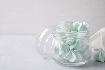 Tasty meringue cookies in glass jar on light grey table. Space for text
