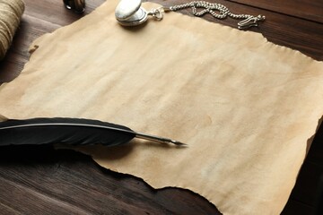 Sheet of old parchment paper, black feather, inkwell and pocket chain clock on wooden table, closeup