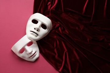 Theater arts. White masks and red fabric on pink background, top view