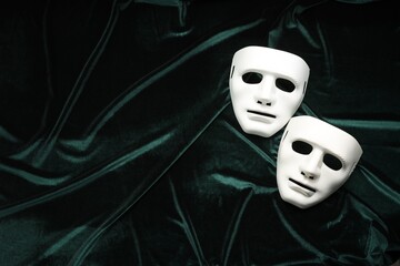 Theater arts. White masks on green fabric, top view. Space for text