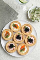 Delicious canapes with salmon, caviar, microgreens and glass of water on beige textured table, flat lay