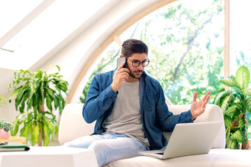 Man sitting at on the sofa at home and using laptop and smartphone for work