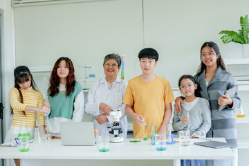 Students' learning in science classroom. Group of students with Asian teacher, smiling, engaging in science class with microscope and laptops on desk, in bright, airy classroom.