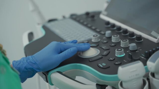 Close-up of doctors hand in protective latex gloves on ultrasound machine during diagnosis in clinic. Doctor in sterile gloves using ultrasound scanner during medical examination. USG machine. 