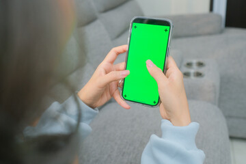 A woman uses a mobile phone or tablet with a green screen to watch videos, surf social media, or have an online conference.