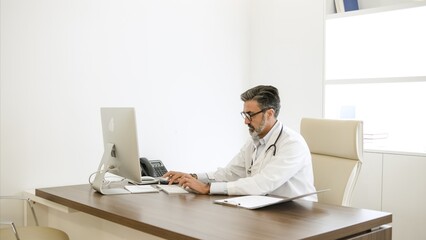 Confident male doctor using computer at desk in clinic