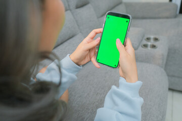 A woman uses a mobile phone or tablet with a green screen to watch videos, surf social media, or have an online conference.