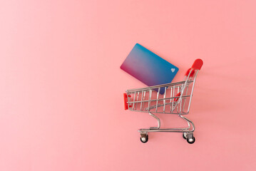 shopping cart with credit cart on pink background