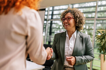 African American woman from Human Resource congratulates the new ginger employee of their company after the job interview.