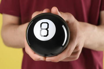 Man holding magic eight ball on yellow background, closeup