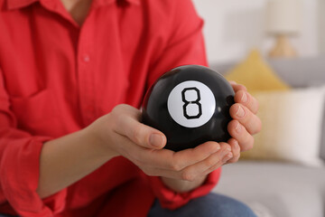 Woman holding magic eight ball indoors, closeup