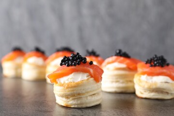 Delicious puff pastry with cream cheese, salmon and black caviar on grey table