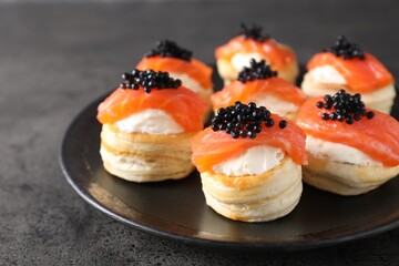Delicious puff pastry with cream cheese, salmon and black caviar on grey table, closeup