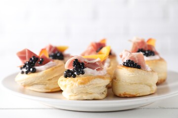 Delicious puff pastry with cream cheese, ham, black caviar and peach on white wooden table