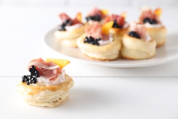 Delicious puff pastry with cream cheese, ham, black caviar and peach on white wooden table