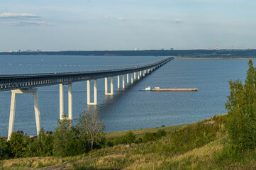 Fototapeta premium A large presidential double-deck girder bridge over the Volga River near city Ulyanovsk. Barge floating under bridge on the river. The longest bridge in Russia and longest girder bridge in the world.